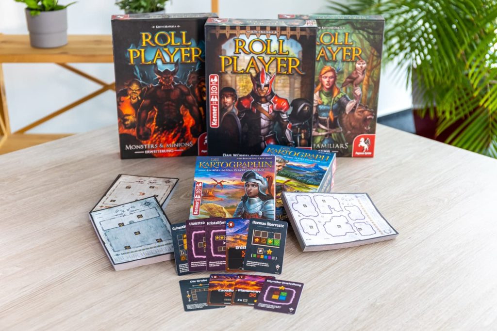 Das Brettspiel Roll Player mit den beiden Erweiterungen Monsters & Minions und Fiends & Familiars und das Brettspiel Die Kartographin