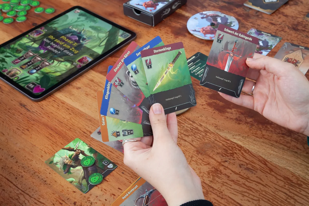 Spielrunde des Brettspiels Boss Fighters QR mit Karten und digitalem Bosskampf auf dem Tablet